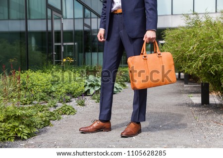 Young businessman standing in front of his company with suit and leather bag, fashion photography