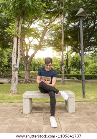 Young Business man use the tablet and sit on the chair in park.