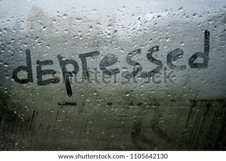 Handwritten word depressed on fog up glass window with rain drops in cold dark tones, illustrates sad emotions, unhappy feelings, loneliness and sadness mood