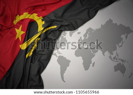 waving colorful national flag of angola on a gray world map background.