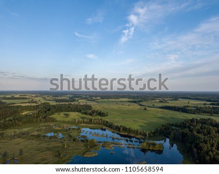 drone image. country lake surrounded by pine forest and fields from above. summer day in swamp area in Latvia