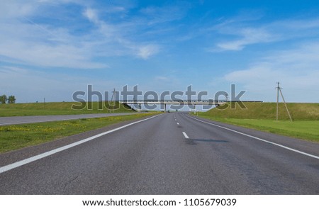 Wide road, green trees and blue sky with gray clouds