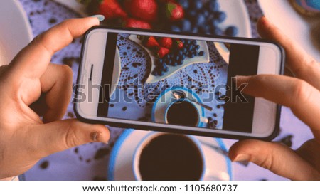 A girl or a woman takes a photo of food, breakfast, coffee, strawberries, coffee.	