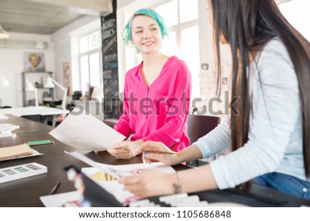 Portrait of two contemporary young women drawing sketches with watercolors  on creative design project in small atelier studio, focus on smiling young woman with mint hair, copy space