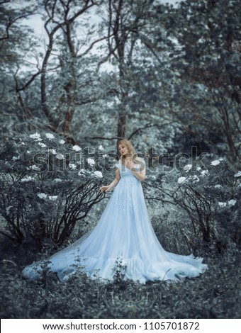 A beautiful blonde girl, a model size plus, walks in a botanical, blooming garden against the backdrop of a pioneering peony. The girl has a luxurious, lush blue dress, like a princess. Art Photo.