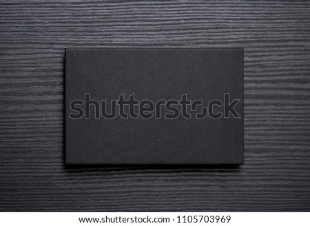Mockup of blank textured black business card on dark wood background