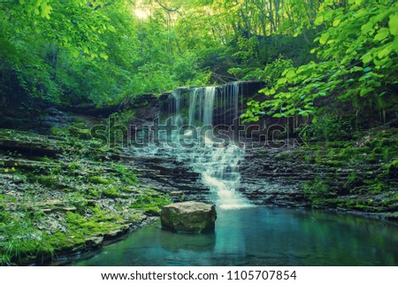 Beautiful mountain rainforest waterfall with fast flowing water and rocks, long exposure. Natural seasonal travel outdoor background in hipster vintage style