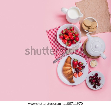 Delicious breakfast with fresh croissant and ripe berries on pink background. Plate with fresh strawberry and cherry. Top view.