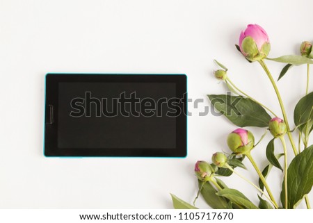 Tablet and buds of pink peonies on the table. Place for text. Office background.