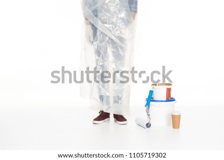 cropped image of man in polyethylene cover standing near paint tins, paint roller and coffee cup isolated on white background 