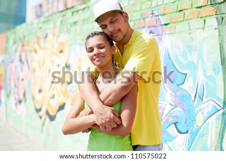 Image of young guy embracing his girlfriend on background of graffiti wall