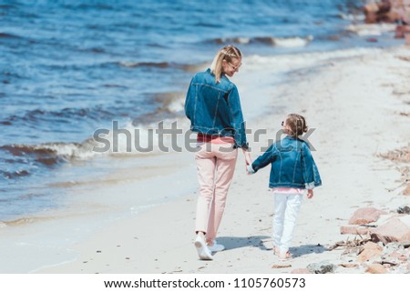 rear view of mom and daughter holding hands and walking on sea shore