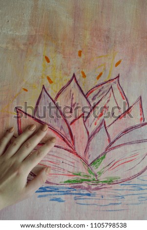 Female hand on the picture of a lotus flower. Figure of the lotus with watercolor on the wall. Hand on a painted old wall.