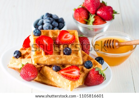 Photo of fresh homemade food made of berry Belgian waffles with honey, chocolate, strawberry, blueberry, maple syrup and cream. Healthy dessert breakfast concept with juice. 