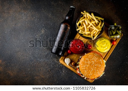 Various party food, Hamburgers, French fries, potato chips, pickled cucumbers, onions, tomatoes and cold beer bottles, rusty black concrete background copy space