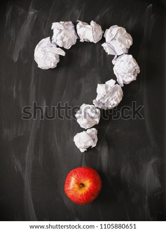 Question mark of crumpled paper with a red apple on a blackboard