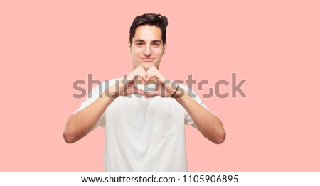 young handsome man smiling, looking happy and in love, making the shape of a heart with hands.