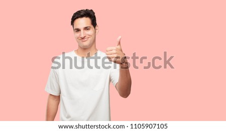 young handsome man with a satisfied, proud and happy look with thumbs up, signaling OK with one hand, sending a positive, "alright' message.