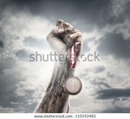 Male hand holding gold medal against the dramatic sky Royalty-Free Stock Photo #110592482