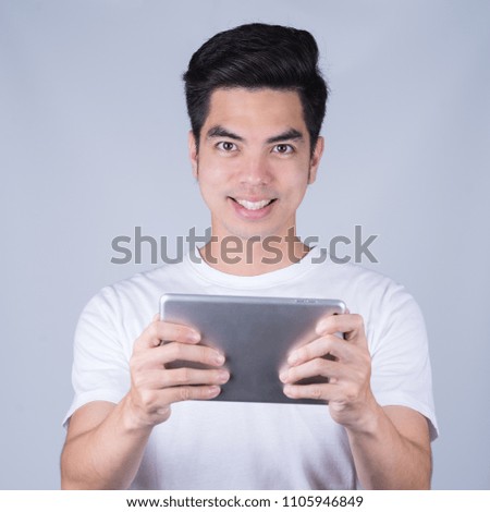 Close up handsome young asian man wearing a white T-shirt holding smart phone or tablet smile and looking isolated on gray  background. Asian man people.  business success concept.