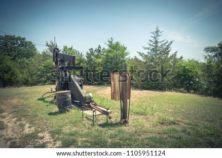 Vintage tone rustic working pump jack pumping crude oil out of well. Pumper, water emulsion at oil drilling site in Gainesville, Texas, US. Old pump jack, oil tanks for Energy, Industrial background