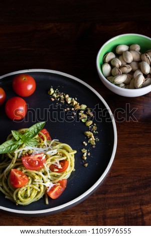 Black plate full of spaghetti with pistachio pesto, toped with cherry tomatoes and cheese