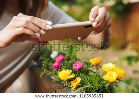 Close up of a girl taking a picture of flowers with mobile phone while standing outdoors