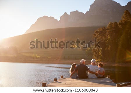 Grandchildren With Grandparents Sitting On Wooden Jetty By Lake Royalty-Free Stock Photo #1106000843