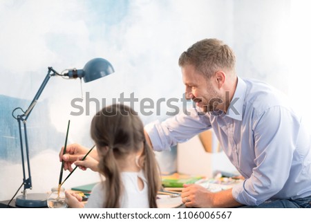 Young father teaching daughter to draw a picture. Happy time together. Setup studio shooting.