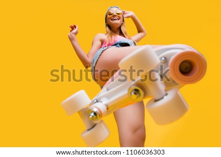 Bottom view of roller skate step on camera, cheerful joyful playful funky girl showing equipment for fitness workout isolated on yellow background