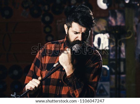Music and leisure concept. Man with enthusiastic face holds microphone, singing song, karaoke club background. Musician with beard and mustache singing song in karaoke. Hipster likes to sing in club.