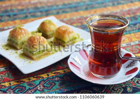 Black traditional Turkish tea with pistachio baklava set of delicious dessert, hot beverage during Ramadan holy month, closeup object blurred background on colorful tradition tablecloth