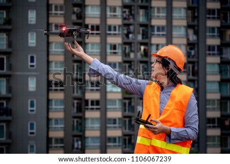 Young Asian engineer flying drone over construction site. Using unmanned aerial vehicle (UAV) for land and building site survey in civil engineering project.