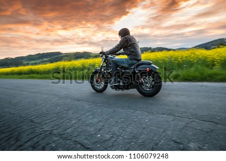Man riding sportster motorcycle on countryside during sunset. Royalty-Free Stock Photo #1106079248