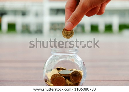 Hand pick up coin over ball shaped coin container