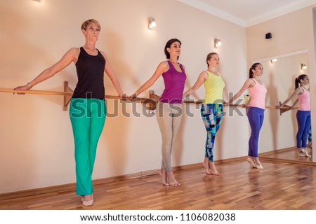 Beautiful adult women doing exercises on stretching ballet barre in Pilates class. Group of females doing yoga, pilates and fitness exercise indoors in studio. Royalty-Free Stock Photo #1106082038