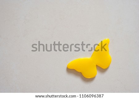 Close up small yellow plastic butterfly toy decorate on grey concrete wall in bathroom.
