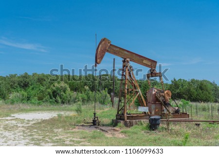 Close-up working pump jack is pumping crude oil and water emulsion at oil drilling site in rural Gainesville, Texas, US. Old pump jack and oil tanks for Energy and Industrial background. Royalty-Free Stock Photo #1106099633