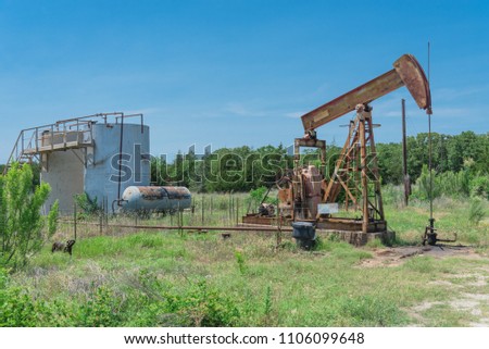 Rustic working pump jack pumping crude oil out of well to tank. Pumper and water emulsion at oil drilling site in Gainesville, Texas, US. Old pump jack, oil tanks for Energy and Industrial background Royalty-Free Stock Photo #1106099648