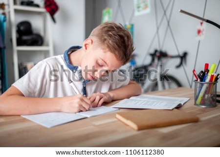 Focused preteen boy doing homework on desk in his room Royalty-Free Stock Photo #1106112380