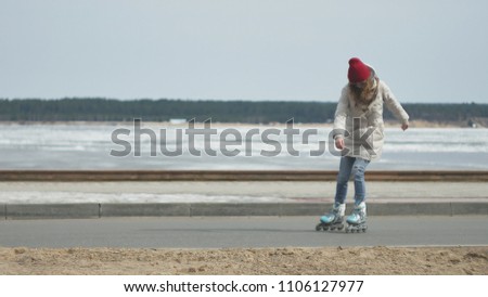 Young beautiful woman in a red hat, wearing sporty warm clothes and rollers, riding on the road on the coast 4k