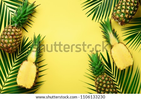 Pineapples and tropical palm leaves on punchy pastel yellow background. Summer concept. Creative flat lay with copy space. Top view.