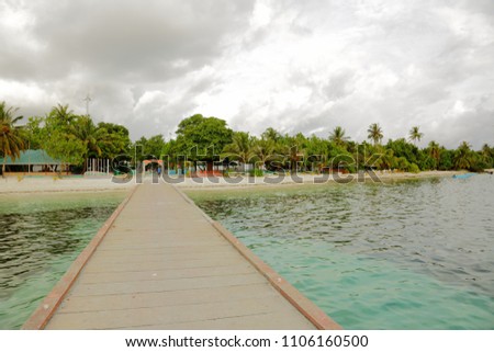Beautiful view of island coast with wooden pier over turquoise water. Green trees and white clouds on background. Maldives, Dhangethi Island, Indian Ocean.