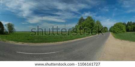 Wide road, green trees and blue sky with gray clouds
