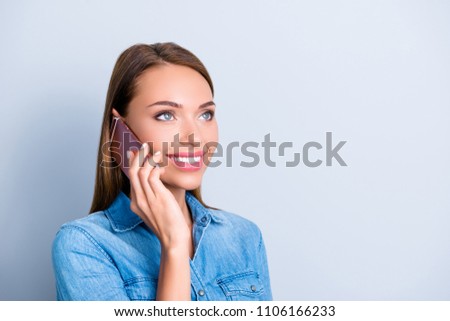 Portrait with copy space, empty place for advertisement of friendly glad girl in jeans shirt holding smart phone near ear speaking with her lover isolated on grey background