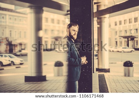 Blond man with a beard in a blue suit strolling on the streets of the city with vaping device. Toned image. success confidence lifestyle concept. portrait of a man working in an office on a city walk