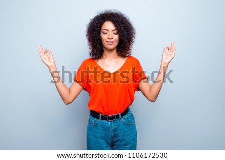 Portrait of delightful pleased woman keeping eyes closed standing in meditative position making yoga practice isolated on grey background