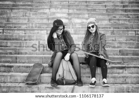 A young hipster girl is riding a skateboard. Girls girlfriends for a walk in city with a skateboard. Spring sports on the street with a skateboard.

