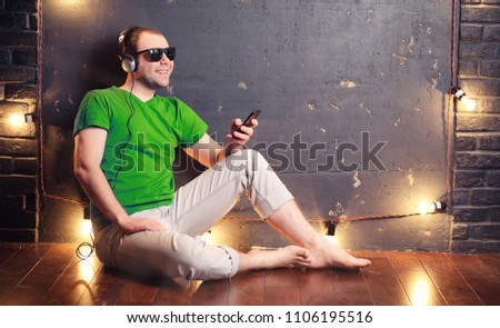 Young man listening to music with headphones sitting on the floor
