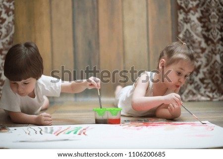 Little children paint on a large sheet of paper on the floor
